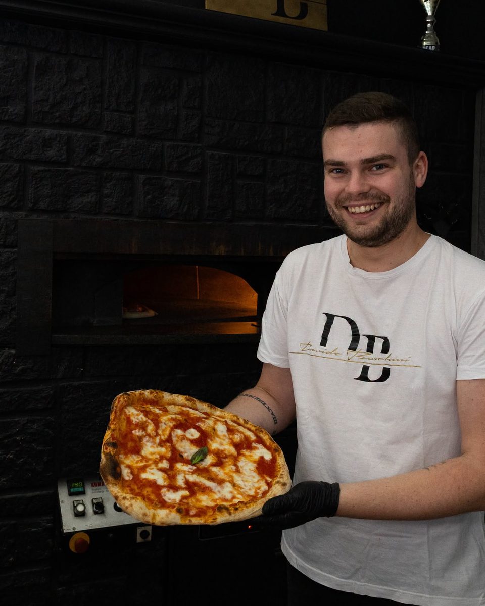 Davide Boschini sorride davanti al forno con una pizza appena sfornata